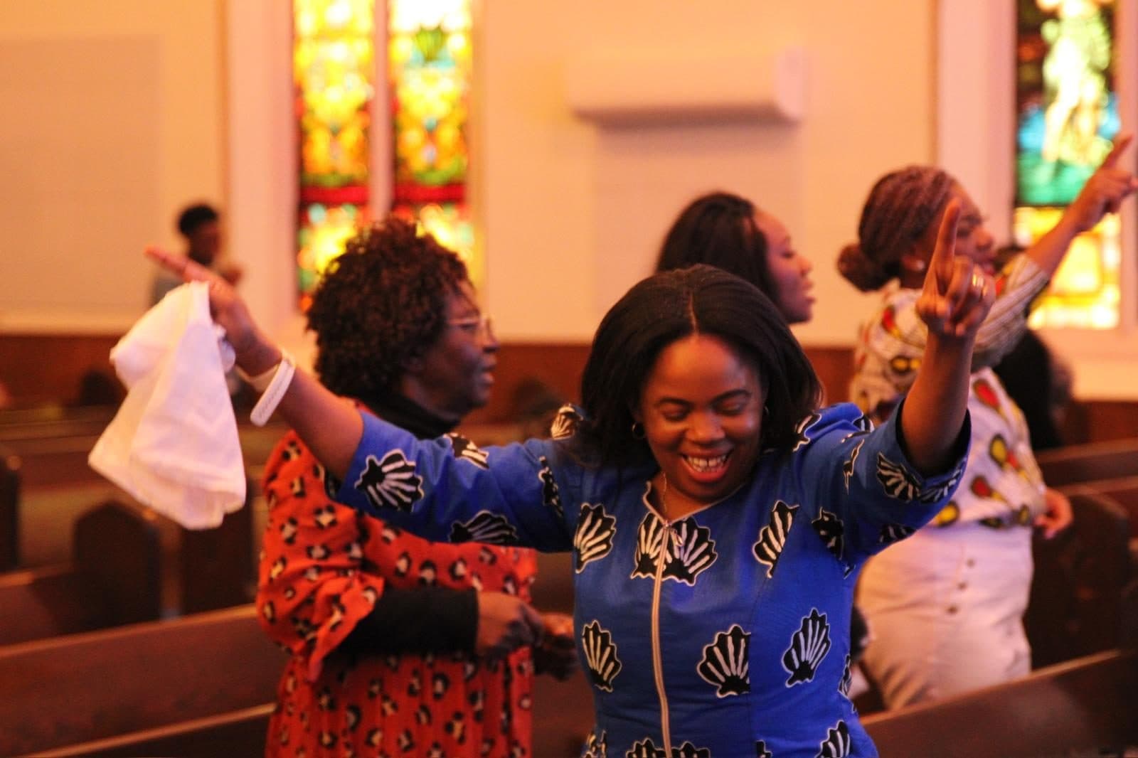 A member worships with hands lifted by the stained glass windows